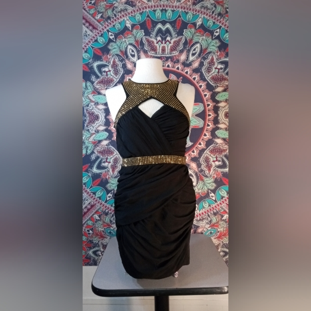 Black mini open chest view cocktail dress with ruched fabric and golden jewels.